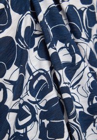 Navy- und weißer Stoff mit floralem Muster, der geschwungene Linien und unterschiedliche Formen aufweist. Das Material wirkt weich mit einer leichten Textur.