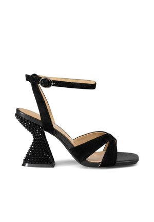 Sandal de tacón alto de ante negro con una amplia correa en el tobillo y un distintivo tacón ancho negro con tachuelas. Diseño de punta abierta.