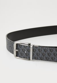 Cintura Calvin Klein con un esterno in tessuto grigio a motivi, retro in pelle nera e fibbia in metallo argento.