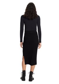 Jupe noire côtelée en tricot avec une fente, portée avec un haut noir à manches longues et des bottines noires épaisses à lacets.