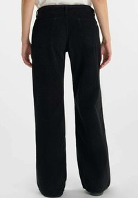 Pantalones de pana negros de pierna ancha con un tejido texturizado, que cuentan con dos bolsillos traseros y una cintura de altura media.