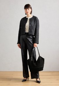 Veste en tweed noir avec des boutons métalliques, top crème, pantalon en cuir noir et un grand sac fourre-tout en daim noir avec des coutures contrastées.