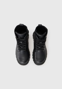 Bottines de combat en cuir noir avec lacets, surface texturée, semelle épaisse et hauteur au niveau de la cheville. Fermeture éclair sur le côté pour un enfilage facile.