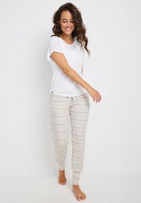 Camiseta blanca de manga corta combinada con pantalones de lounge de rayas pastel, ajustados y con cordón y puños en los tobillos.