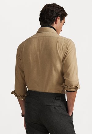 Camisa marrón con mangas enrolladas y una tela texturizada, combinada con pantalones gris oscuro que tienen bolsillos laterales y una cinturilla ajustable.