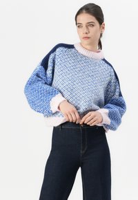Kék és fehér mintás kötött pulóver rózsaszín bordás gallérral és tengerészkék részletekkel, sötét farmer magas derékú nadrággal párosítva.