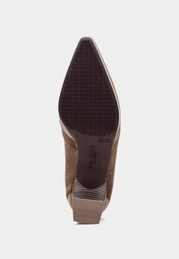 Zapato de ante marrón con un talón texturizado, punta afilada y agarre de caucho en la suela. El diseño presenta rayas horizontales en la parte trasera.