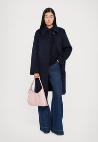 Marineblauwe wollen jas met een kraag, knoopsluiting, gedragen over een donkere trui en wijde denim. Bevat een lichtroze leren tas.