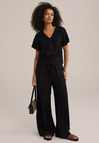 Čierny, krátky rukáv, košeľa s gombíkmi a V-výstrihom; široké nohavice so šnúrkou. Nosí sa s páskovými sandálmi a tkanou kabelkou.