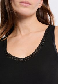 Top nero senza maniche con scollatura a V e bordo in pizzo. Il tessuto è morbido e dalla superficie liscia, evidenziando il design della scollatura e le cuciture.