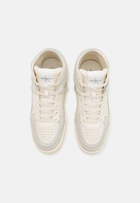 Vysoké tenisky v světle béžové a šedé kůži. Perforovaná špička, šňůrky a detail loga na jazyku. Hladká textura.