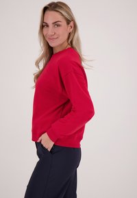 Rode sweatshirt met een ronde halslijn en geribde manchetten, met een losse pasvorm en een gladde textuur; gecombineerd met donkere broeken.