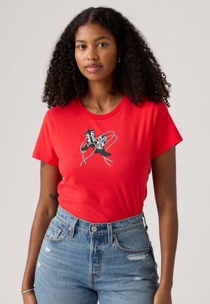 T-shirt en coton rouge à manches courtes, avec un imprimé graphique de chaussures noires et blanches avec des lacets au centre. Encolure classique.