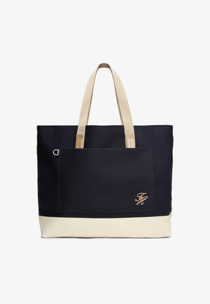 Duża granatowa torba na ramię z kremowymi uchwytami i spodem, zewnętrzna kieszeń na suwak z przodu, z beżowym haftowanym inicjałem.