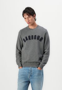 Γκρι φούτερ με σκούρο ναυτικό μπλε κείμενο "BARBOUR". Στρογγυλή λαιμόκοψη, ραμμένες μανσέτες και τελείωμα. Φορεμένο με ανοιχτό μπλε τζιν. Λείος υφασμάτινος υφή.