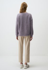 Lila donzige trui met lange mouwen, ronde hals en een losse pasvorm, gecombineerd met beige slim-fit broek en witte sneakers.