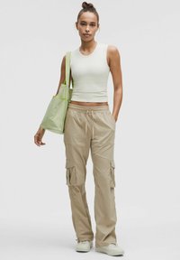 Beżowe spodnie cargo z bocznymi kieszeniami, w połączeniu z jasn zieloną bluzką bez rękawów. Modelka trzyma jasn zieloną torbę na ramię z kontrastowym paskiem.