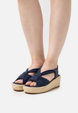 Navy fabric wedge sandals with twisted front straps, natural woven jute platform, and rubber sole, featuring a small branded accent.