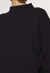 Schwarzer Strickpullover mit hohem Kragen, entspannter Passform und weicher Textur, der Einfachheit im Design betont.