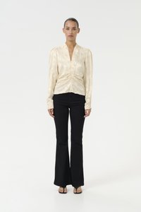 Cream-colored long-sleeve blouse with a deep V-neck and gathered detailing, paired with black flared jeans and simple sandals.