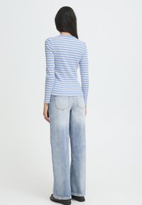 Gestreiftes Langarm-Top in Hellblau und Weiß mit figurbetontem Design. Kombiniert mit hellblauen, weit geschnittenen Jeans und schwarzem Schuhwerk.