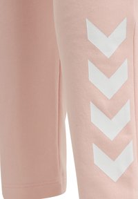 Zbliżenie na jasnoróżową tkaninę z czterema białymi szewronami skierowanymi w dół, nadrukowanymi pionowo po prawej stronie.