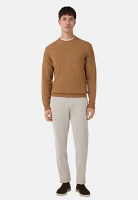 Maglione marrone a maglia con polsini e orlo a costine, abbinato a pantaloni chiari texturizzati e calzature marroni. Design semplice e moderno.