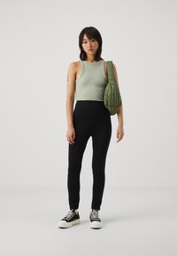 Un haut court côtelé vert associé à un legging noir ajusté et des baskets noires avec des semelles blanches. Le modèle porte un sac en toile vert olive.