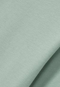Material de culoare verde deschis cu o textură netedă, care prezintă un luciu subtil și o țesătură uniformă, pliat într-un mod suprapus.