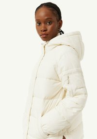 Witte pufferjack met een capuchon, voorzien van gestikte delen, een ritszak op de mouw en elastische manchetten. Glad textuur en minimalistisch ontwerp.