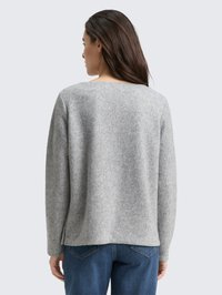 Maglione grigio in maglia con scollo ampio e maniche lunghe, caratterizzato da una finitura testurizzata. Abbinato a jeans di denim blu per contrasto.