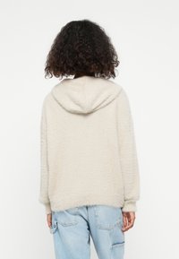 Crèmekleurige hoodie met een fluffy textuur, drop shoulders en geribbelde manchetten, gecombineerd met lichtgewassen denimbroeken.