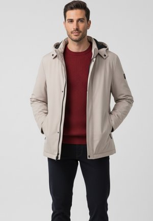 Chaqueta ligera beige con capucha, cierre de cremallera, bolsillos laterales, combinada con un suéter burdeos de canalé y pantalones oscuros. Textura suave.