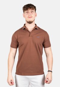Bruine polo met korte mouwen, contrasterende blauwe accenten op de kraag en een kleine geborduurde logo op de borst.