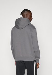 Grå hoodie med en stor huva och vita sidostreck. Har en avslappnad passform med ribbade ärmslut och fåll, tillverkad av mjukt tyg.