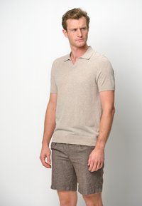 Short-sleeve beige knitted polo shirt with a V-neck and ribbed hem, paired with brown textured shorts featuring a rolled cuff.