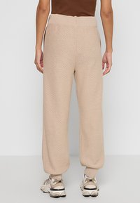 Beige knitted joggers with a textured pattern, elastic waistband, and tapered cuffs, paired with light-colored sneakers.