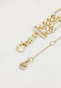 Bracciale in metallo dorato con chiusura ad anello, anelli interconnessi e un piccolo ciondolo circolare inciso con "DKNY."