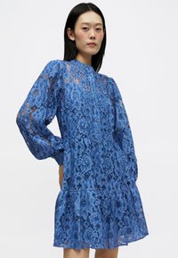 Μπλε δαντελένιο φόρεμα με μακριά φουσκωτά μανίκια, ψηλό λαιμό, λουλούδινη ατμόσφαιρα, κλιμακωτή φούστα με ρυτίδες και ημι-διαφανή υφή.