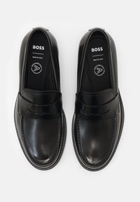 Paire de mocassins pour hommes en cuir noir avec un détail de bride, de la marque "BOSS Made in Italy", vus de dessus sur un fond blanc.