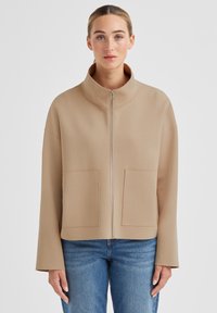 Beige Reißverschlussjacke mit hohem Kragen, zwei Vorder Taschen und weiter Passform. Glatter Stoff mit matter Oberfläche und weiten Ärmeln.