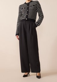 Randig svart och vit cardigan med stora knappar, parat med högmidjade svarta vida byxor och svarta klackar. Slät textur, skräddarsydd passform.