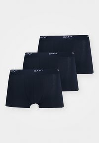 Tre boxer da uomo neri della marca GANT con elastici in vita impilati su uno sfondo chiaro.