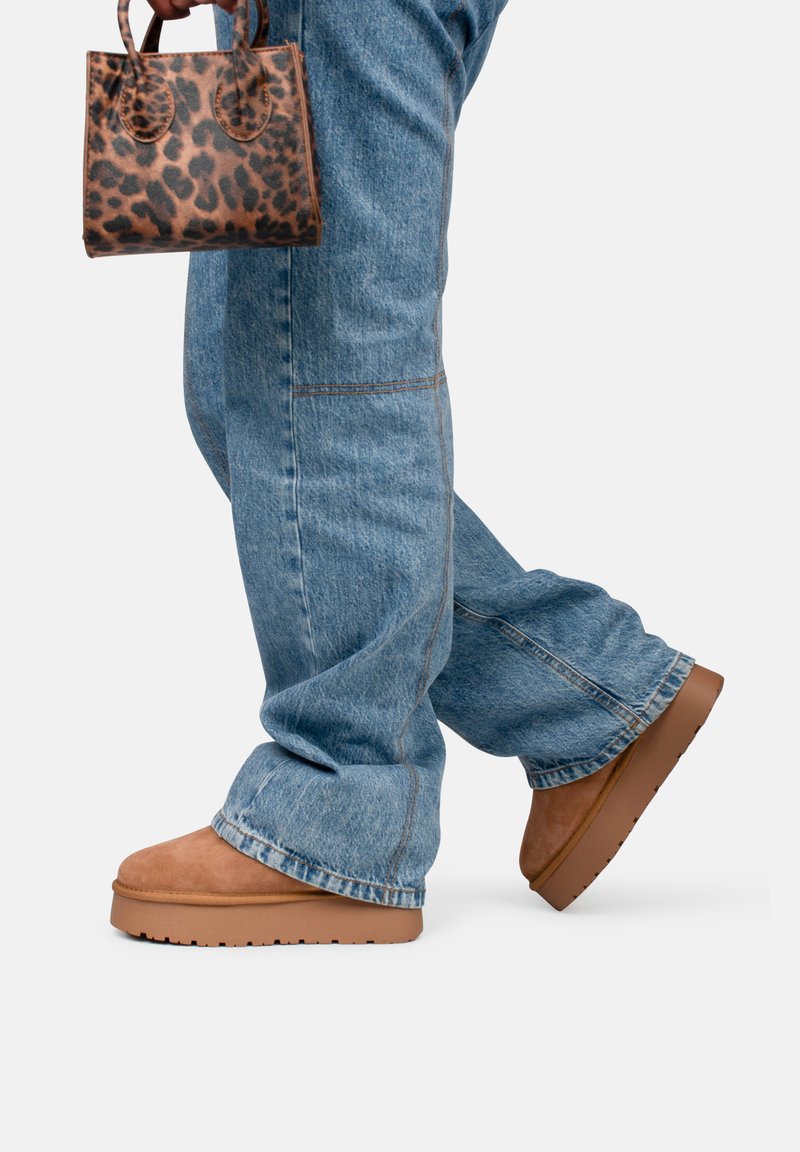 Botas de plataforma de ante marrón, jeans de pierna ancha de color azul claro y un pequeño bolso de mano con estampado de leopardo. Las botas tienen una suela gruesa y una textura suave.