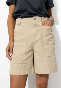 Shorts en coton beige à coupe décontractée, dotés de deux grandes poches latérales, d'un ourlet droit et d'une fermeture à bouton à la taille.