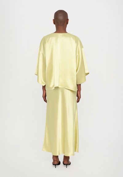 Conjunto de dos piezas fluido de satén en amarillo pálido. La parte superior cuenta con mangas anchas, mientras que la falda es larga y suave, combinada con tacones negros.