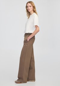 Biały krótki top z krótkim rękawem oraz brązowe spodnie z szerokimi nogawkami i kieszeniami. Spodnie posiadają elastyczny pas oraz subtelne detale zszycia.
