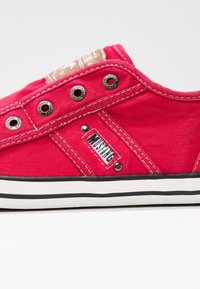 Baskets basses en toile rouge avec semelle en caoutchouc blanche, œillets métalliques, coutures blanches et étiquette de la marque Mustang sur le côté.