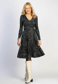 Musta kietaisumekko, jossa on pitkät hihat, kullan- ja hopeanvärinen paisley-kuvio, liehuva hameosa, yhdistetty polveen ulottuviin valkoisiin saappaisiin, sileä pinta.