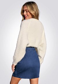 Witte fuzzy cropped trui met open brei-textuur, gecombineerd met een blauwe denim minirok, die een getailleerd silhouet en zichtbare zoom laat zien.